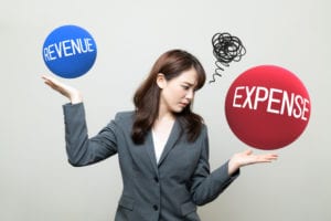Woman in business attire balancing two balls one of expenses in red and revenue in blue.