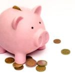 Pink piggy bank with scattered coins on white background.