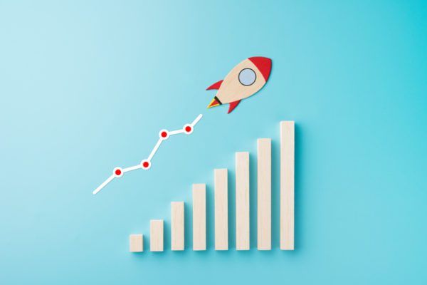 A paper rocket ascending along a growth chart on a blue background.