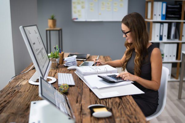 Woman working at a desk with a computer and documents in a modern office setting.