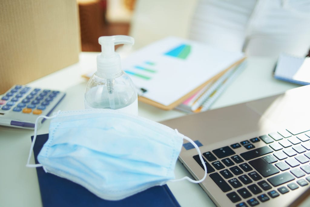 Closeup on medical mask and hand disinfectant on the table in temporary home office during the coronavirus epidemic in the living room in sunny day.