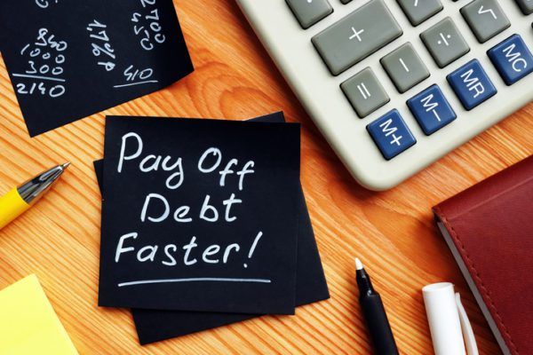 A note with "pay off debt faster!" written on it, alongside a calculator, pens, and financial documents on a desk.