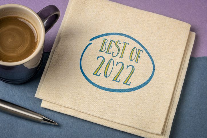 A coffee cup next to a book titled "best of 2022" with a pen on a blue surface.