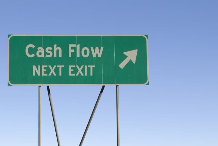 Green road sign with the words Cash Flow Next Exit and a blue sky gradient background.