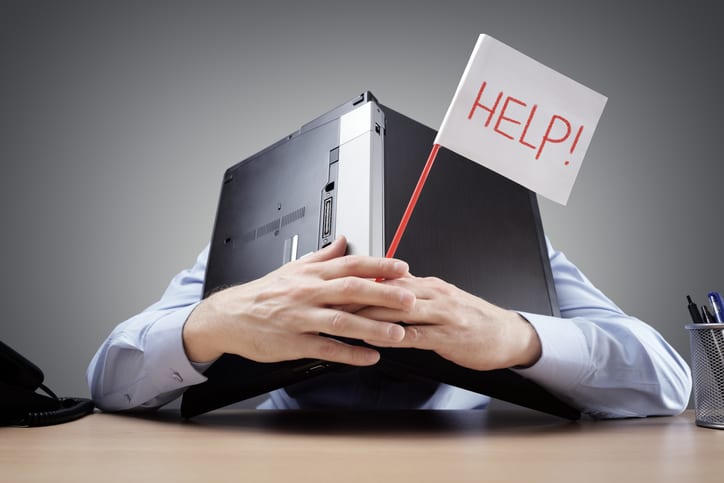 Frustrated and overworked businessman burying his head under a laptop computer asking for help