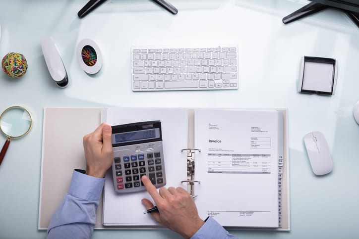 Elevated View Of A Businessperson's Hand Calculating Bill On Desk At Workplace