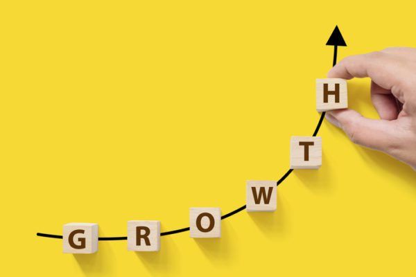 Hand arranging wooden blocks spelling "growth" on an upward trajectory against a yellow background.