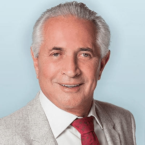 Mature man Henry Wozow with silver hair wearing a suit and red tie against a blue background.