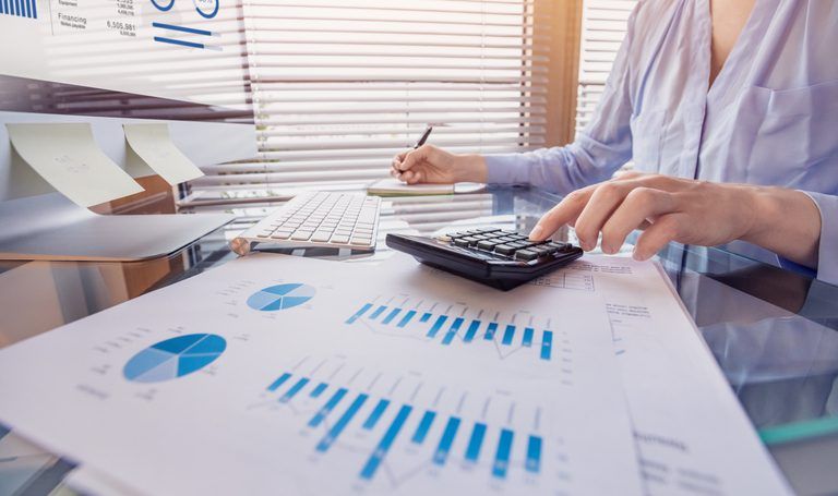 A person analyzing key strategies to maximize working capital with charts on paper while using a calculator and a computer in an office setting.