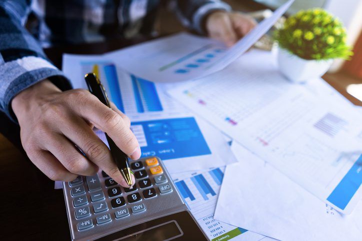 Person analyzing financial data and using a calculator to do calculations with charts and graphs on the table for working capital management.