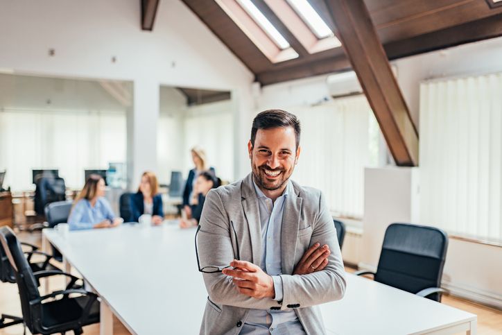 Image of a smiling confident business man with crossed arms in a conference room.