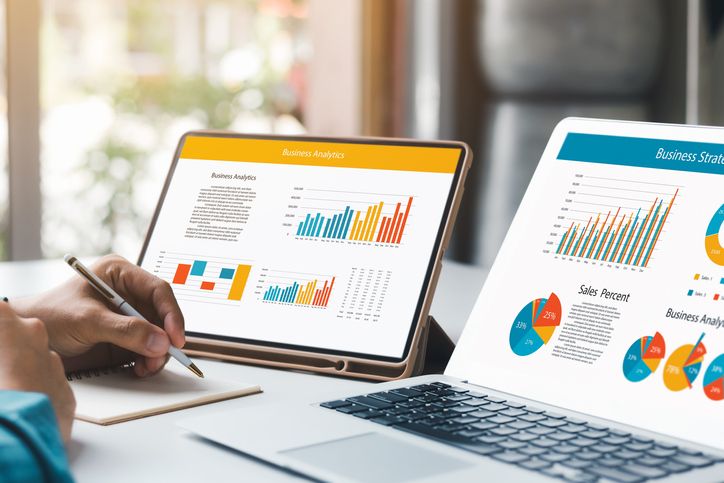 Person reviewing business analytics and strategy charts on a digital tablet with a stylus to maximize business cash flow, next to paper reports with similar graphs.