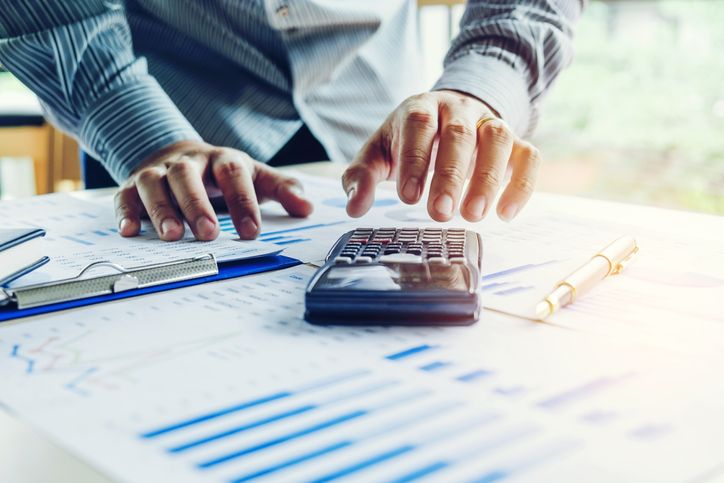 A person addressing accounts receivable issues using a calculator over financial documents on a desk, with a pen and notebook present.