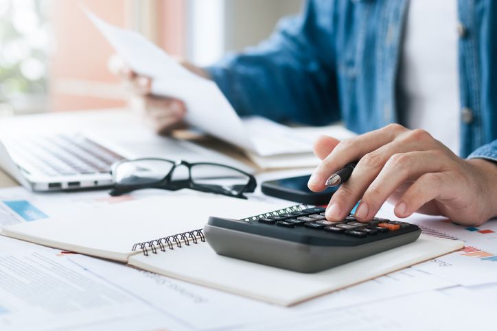 Person using a calculator to analyze the accounts receivable turnover ratio and reviewing documents at a desk with eyeglasses and papers.