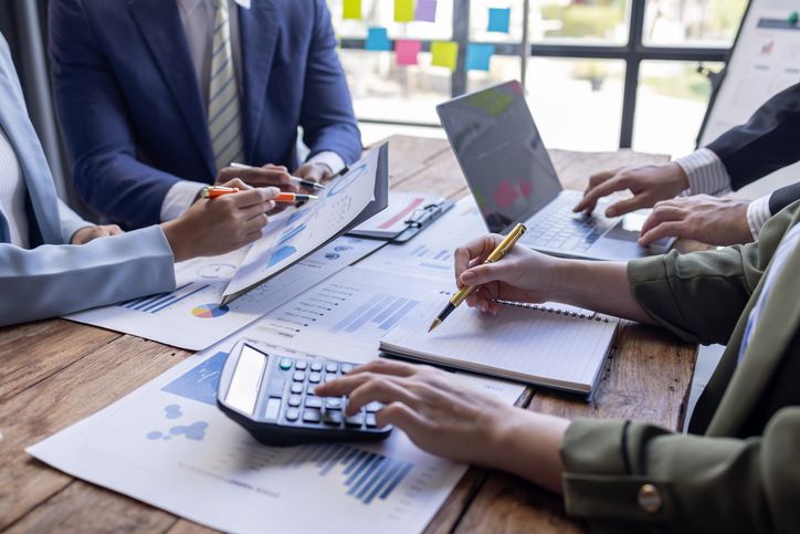 Group of business people point to graphs and charts to analyze top finance solutions to plan new sales strategies to increase production capacity.