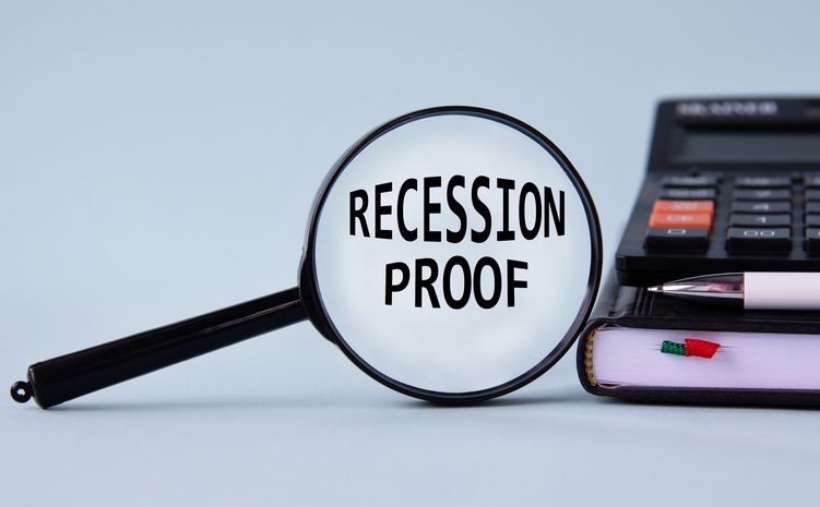 RECESSION PROOF - words on magnifying glass on a light background with calculator, notepad and pen. Business and finance concept