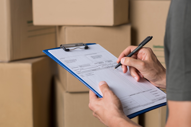 Manager chcing wholesale invoice with cardboard box parcel in background.