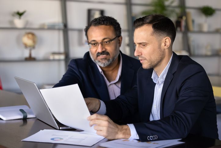 Two focused businessmen working together at office desk, analyzing best business funding otptions.