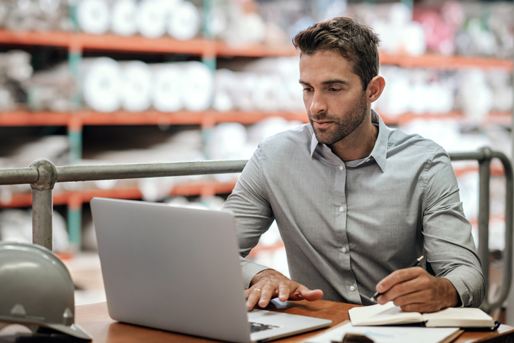 B2B business owner in a warehouse reviewing working capital and cash flow on a tablet.